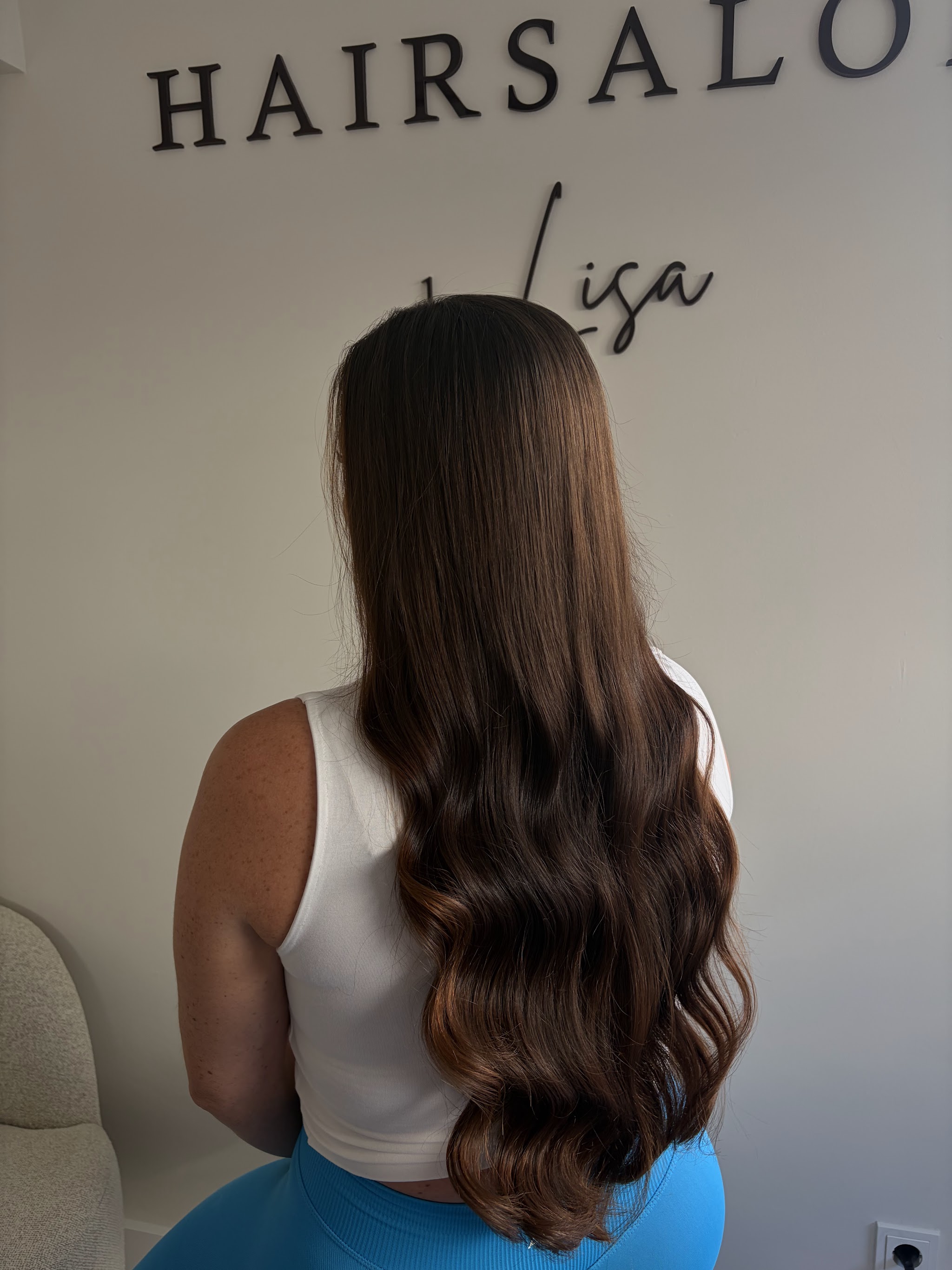 Lang donkerbruin haar met golven in de punten, van achteren gezien onder de muurletters Hairsalon by Lisa